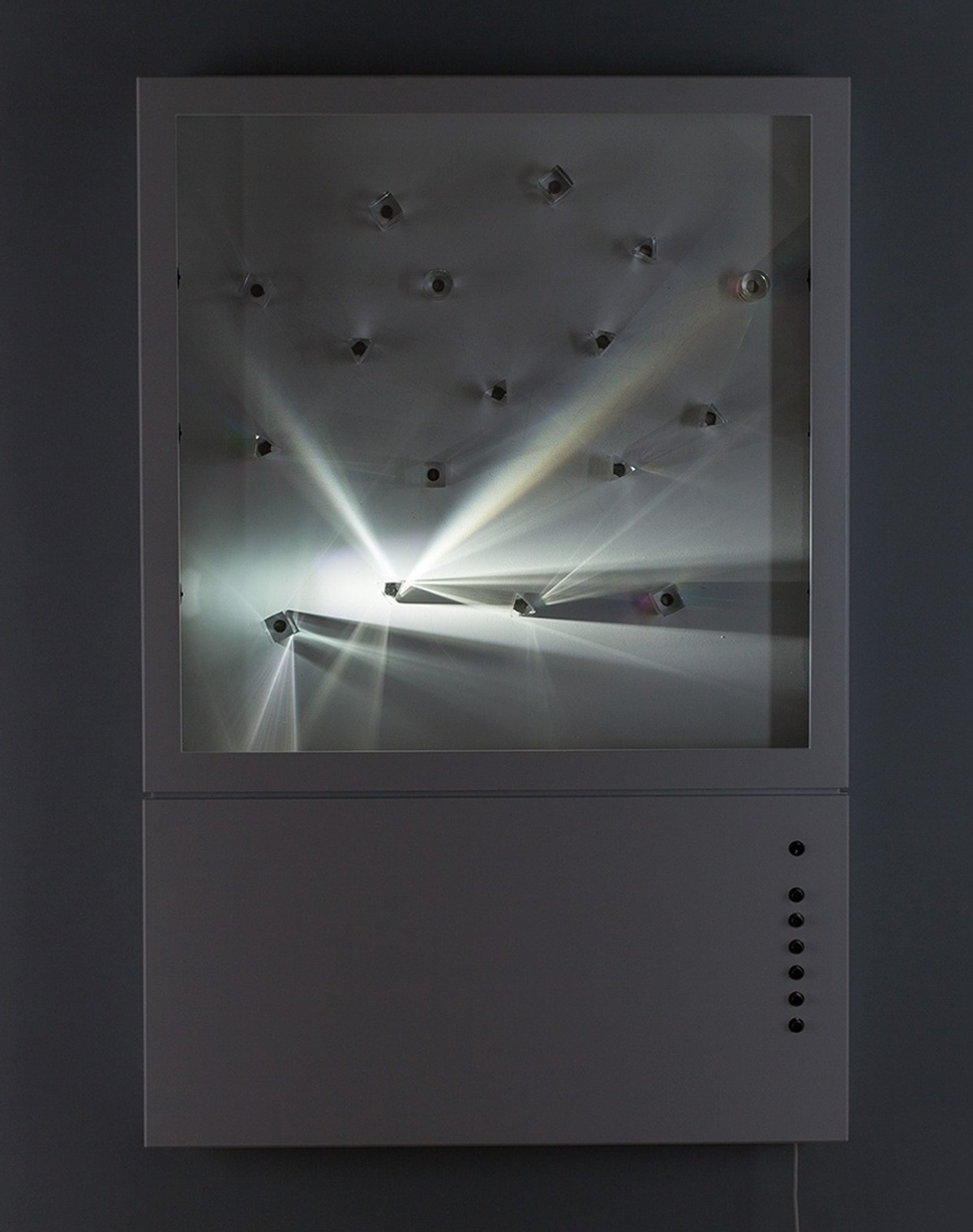A rectangular device containing a blank "canvas", transparent prisms and one light that emits from one point in the frame, creating angular rays of white light to disperse outward