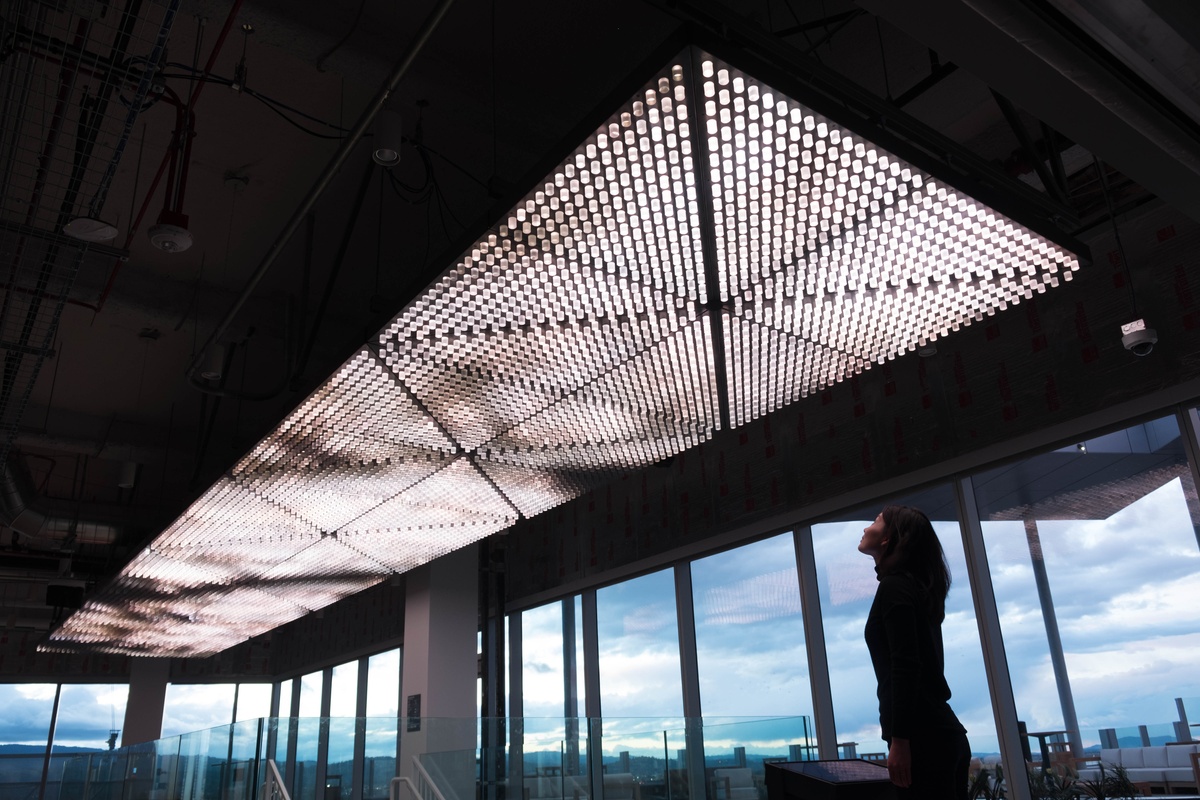 Young woman looking up at celing installation, composed of repeated light modules and displaying light patterns