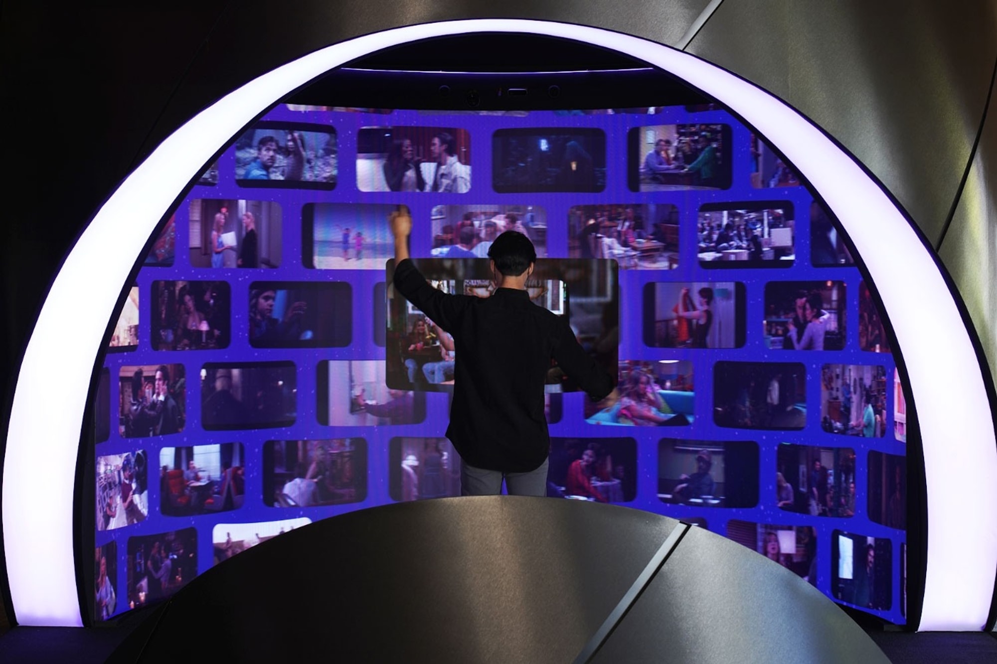 Person standing inside the HBO experience with their arms raised and video clips on purple digital surface