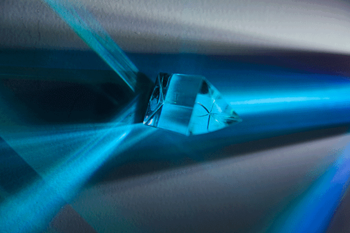 Prism rotating on black surface in blue light, causing streams of changing blue light to rotate on the surface