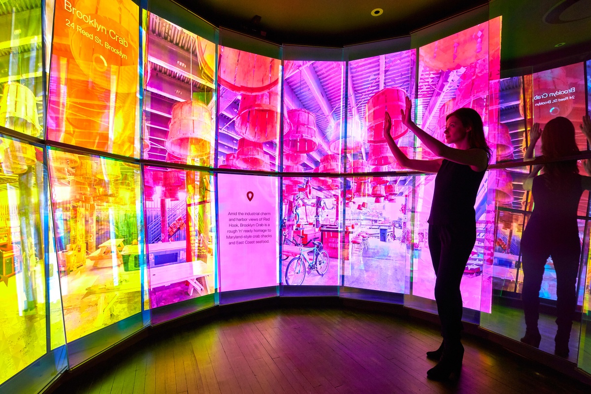 Woman moving her hands, interacting with The City Cave, whose screen shows a stylized version of a location in Brooklyn