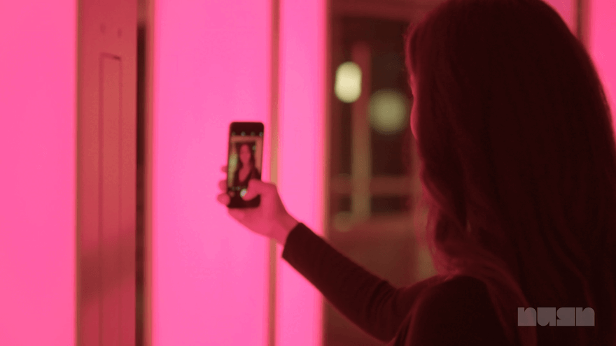 Video of woman taking selfie in front of pillars, and photo appearing on phone