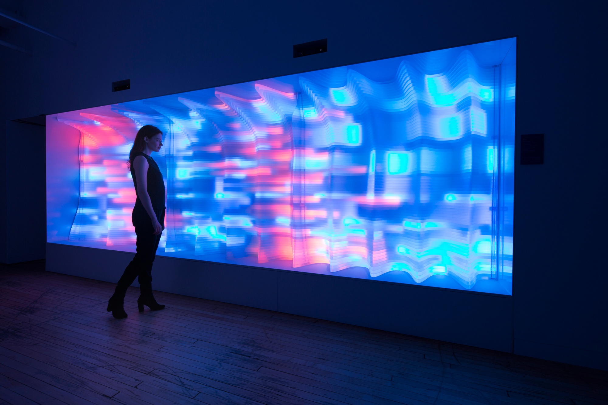 Woman looking at The Passage, composed of glowing pink and blue layers, which convey depth and light