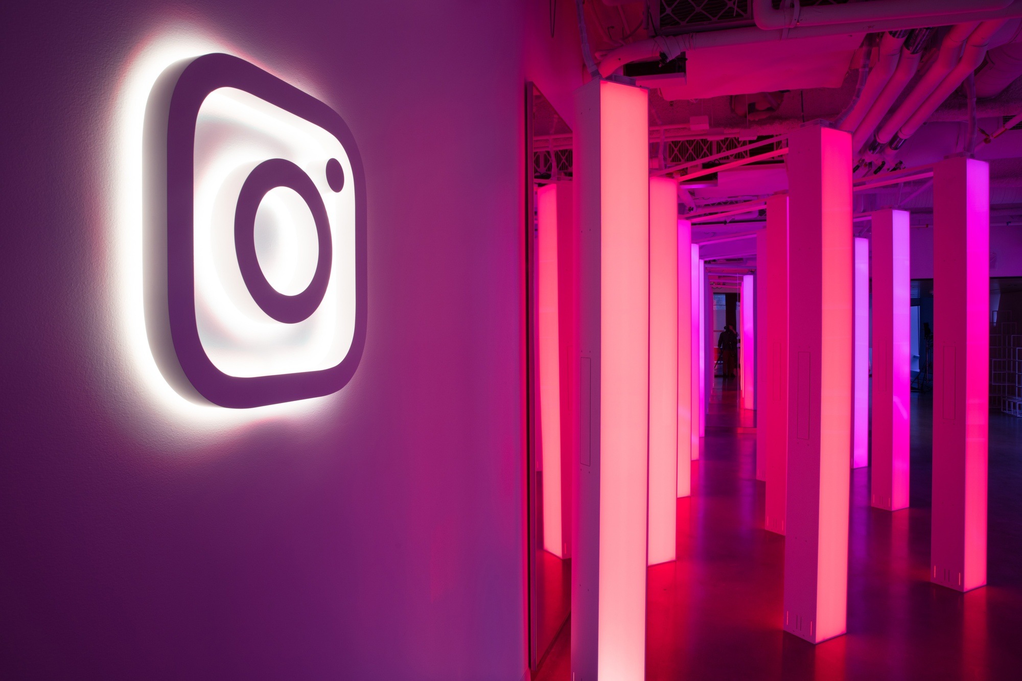 Illuminated Instagram Logo with light pillars behind with pink gradient