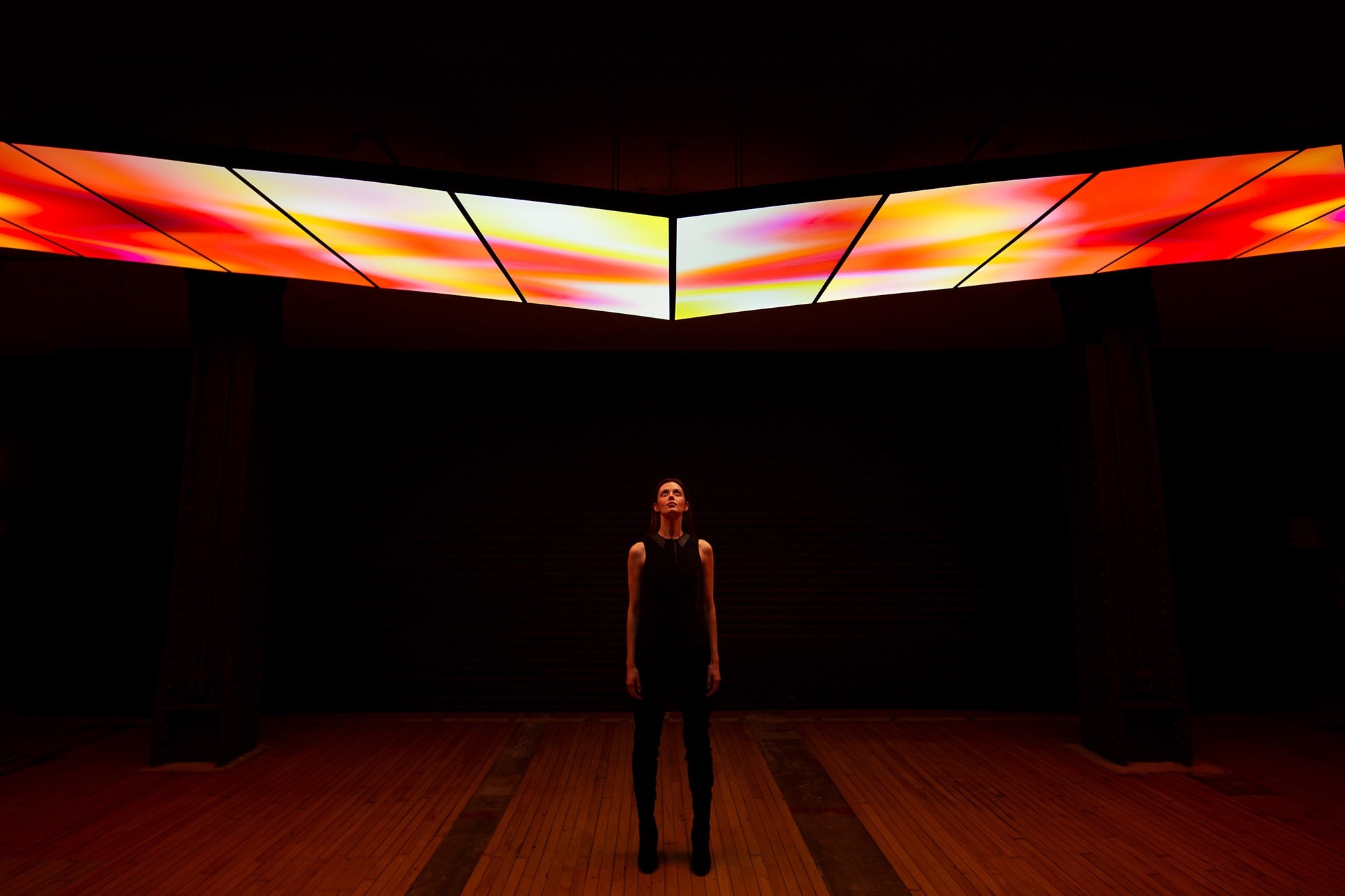 Woman standing under angled digital surfaces with abstract content running across