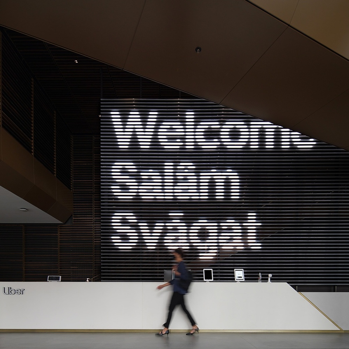 Woman walking past front desk with welcome message on light tubes