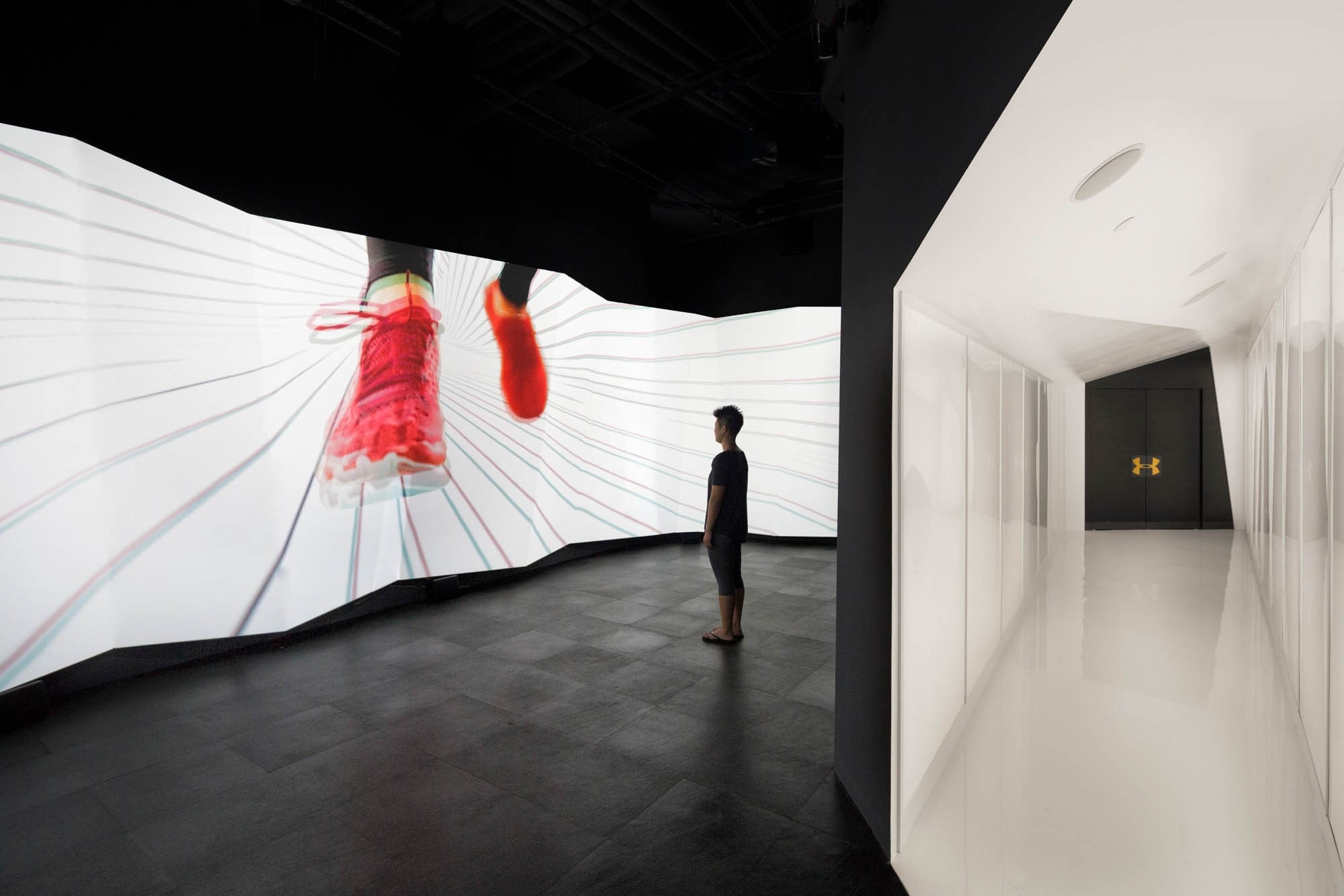 View of person standing in front of angular digital surface with red shoes, and a white angled hallway