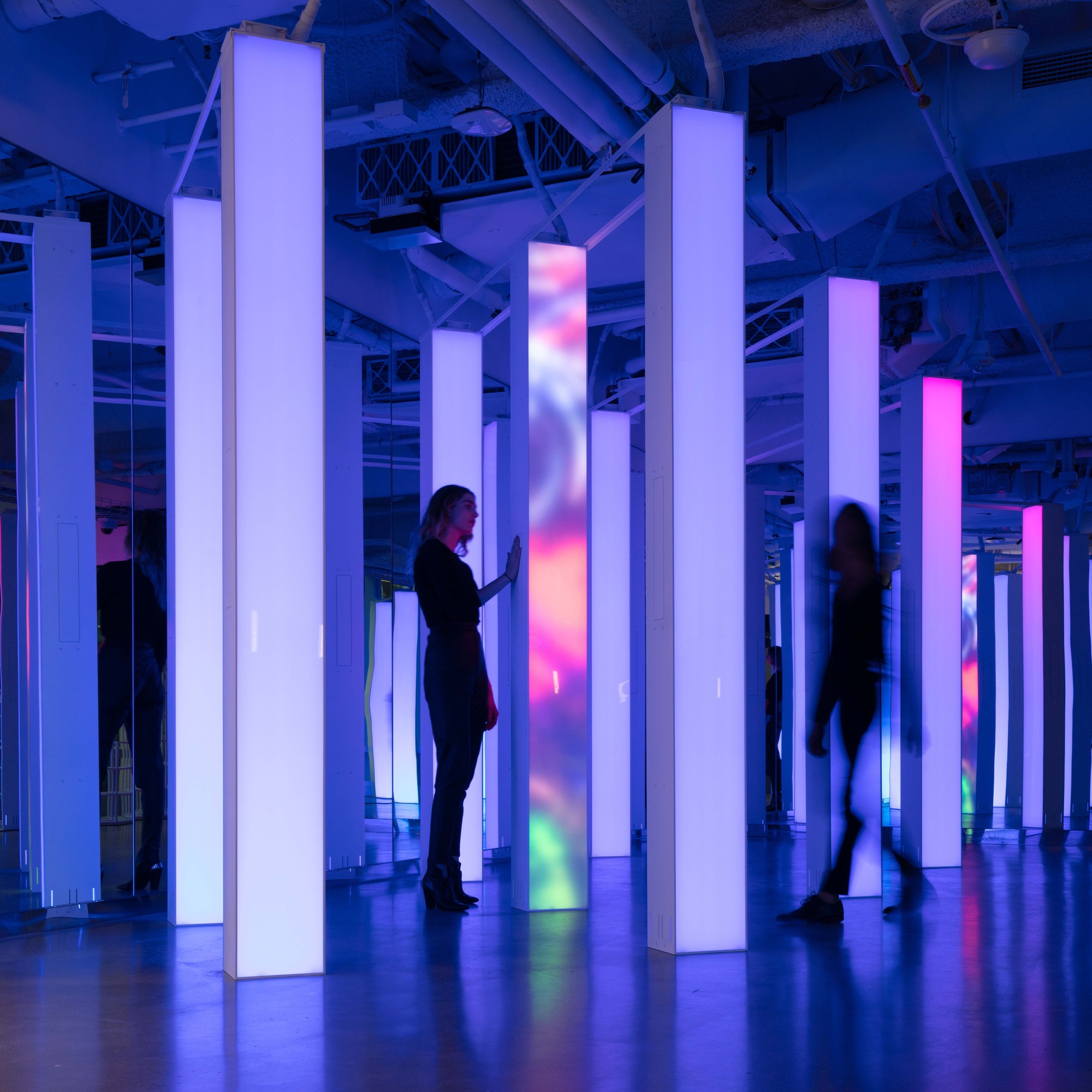 Two women standing between digital pillars with light purple gradient.