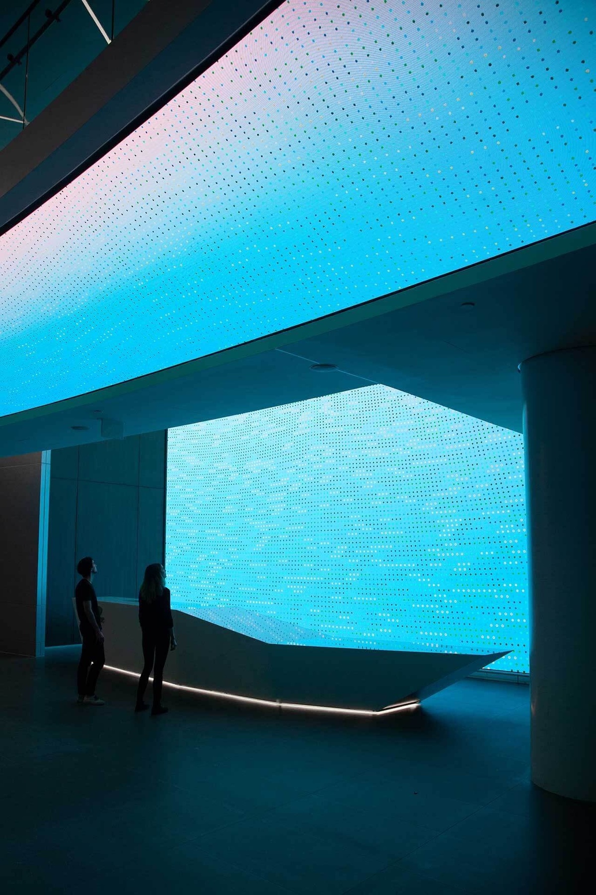 Photograph of finished environment, with data visualization patterns on large screen that covers the wall of the space and runs above the heads of people