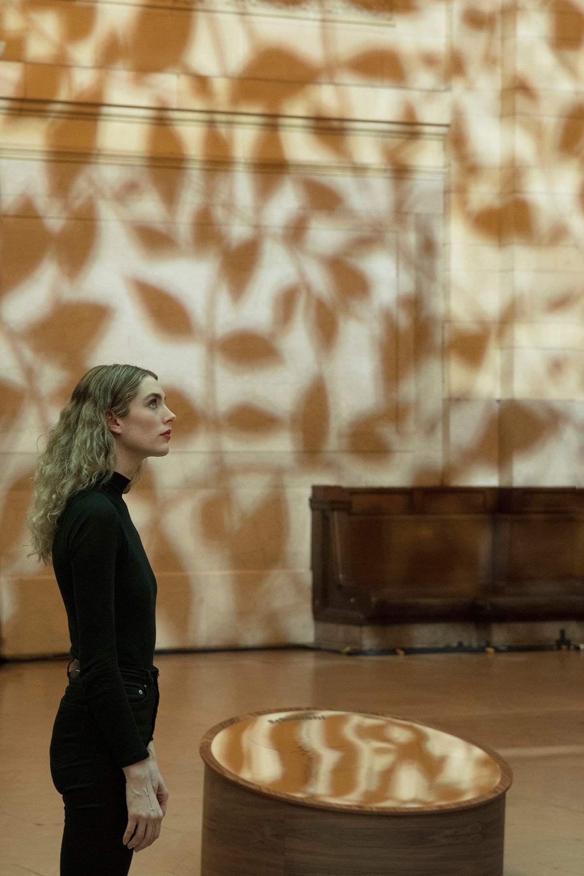 Young woman looking up at the Giving Tree while it produces lighting that imitates dappled sunlight and projects shadows of branches onto the walls