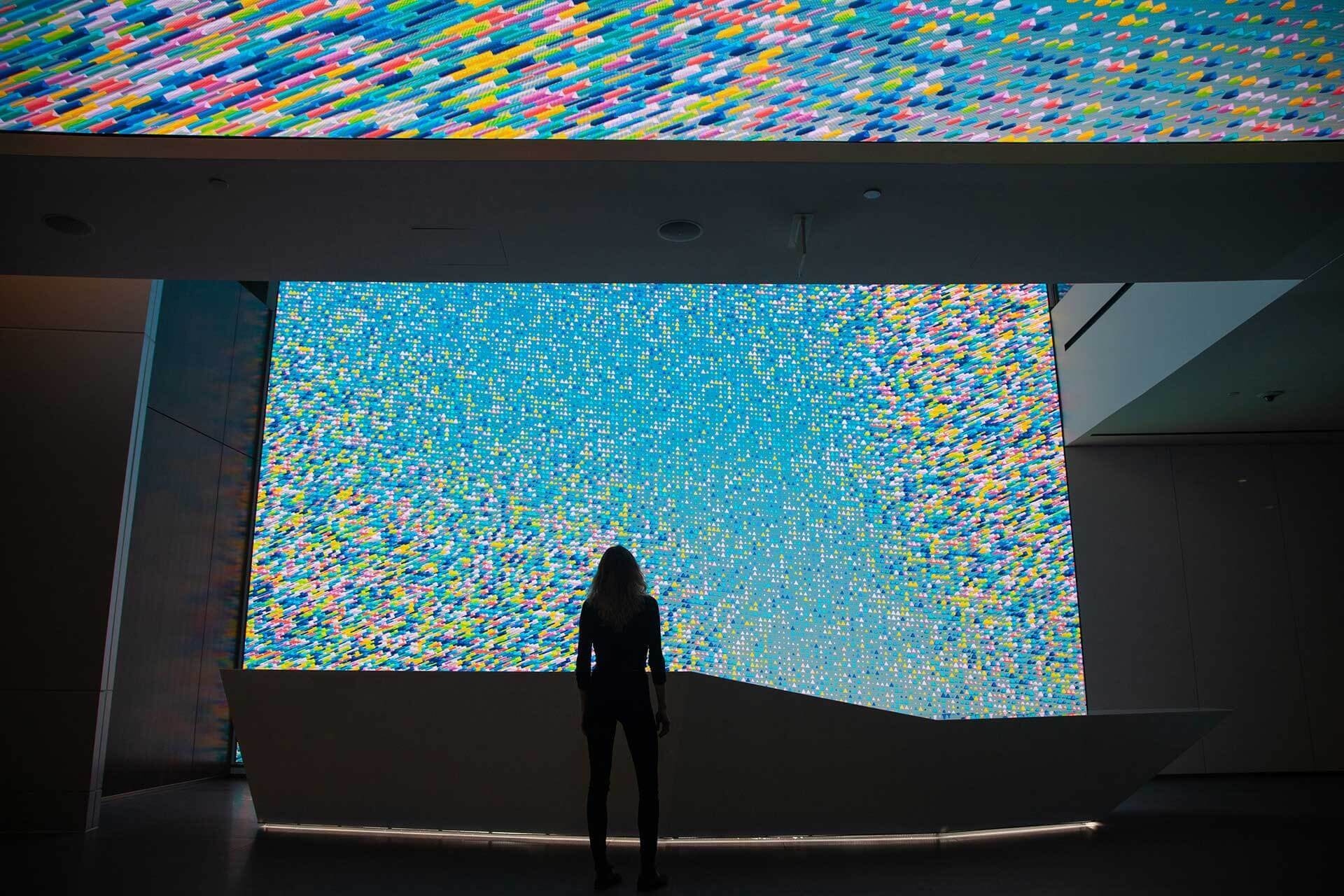 Silhouette of a woman standing in front of a large LED screen with animated graphic patterns that showcase internal and external company data insights