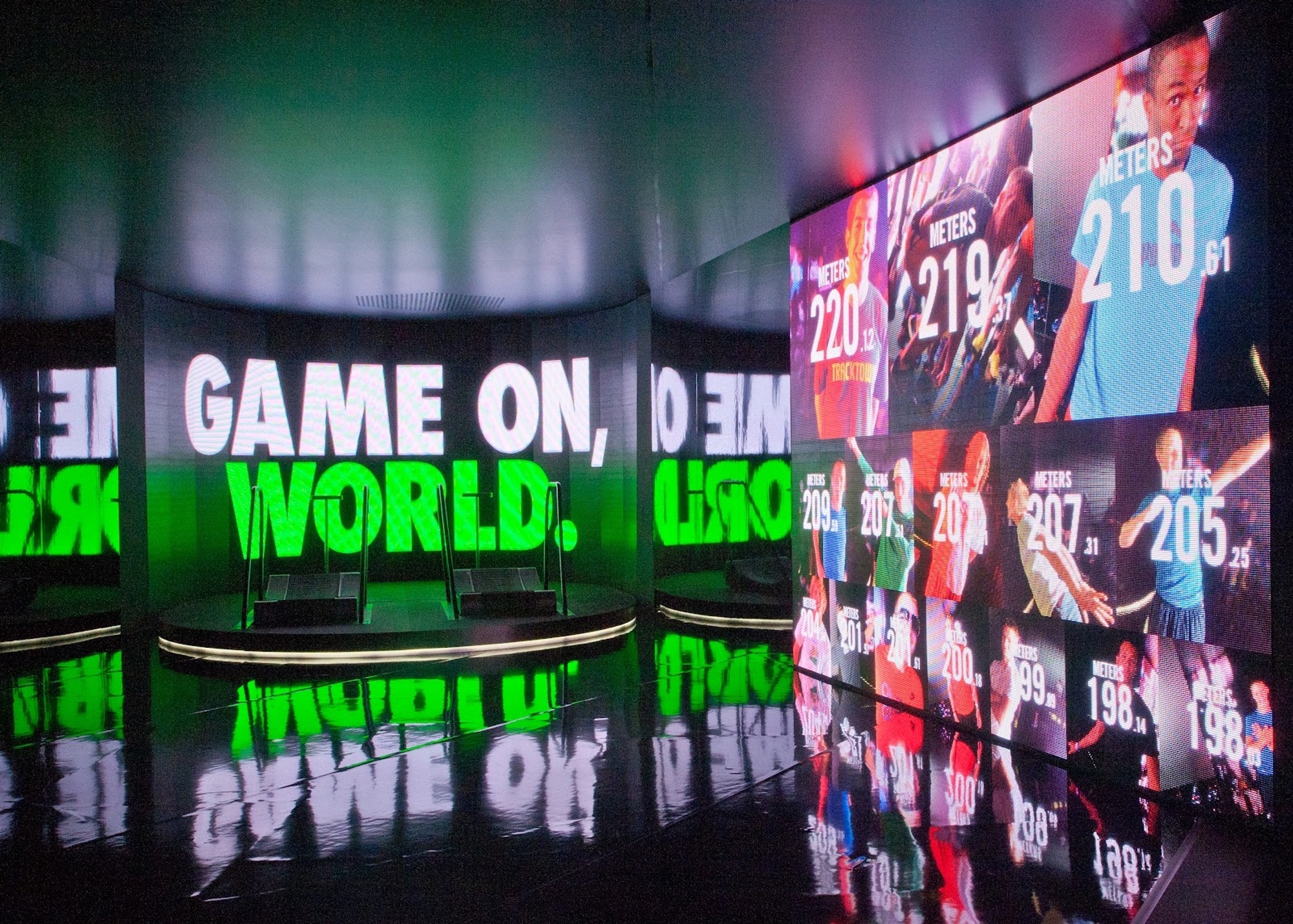 Treadmills on a raised platform beside a wall that displays a leaderboard of the top results of participating runners