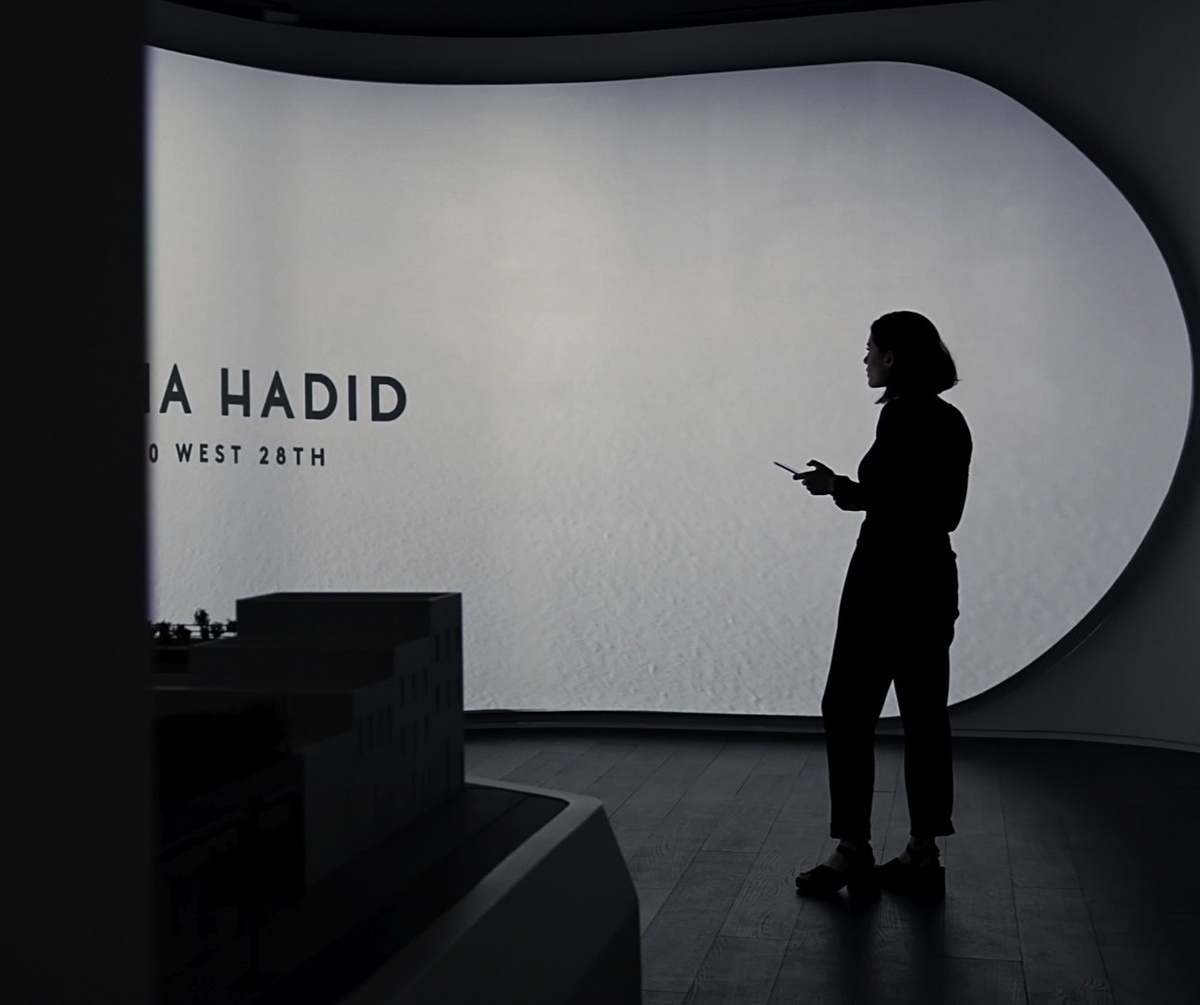 Woman with mobile device standing in front of a rounded shape that displays the words "Zaha Hadid"