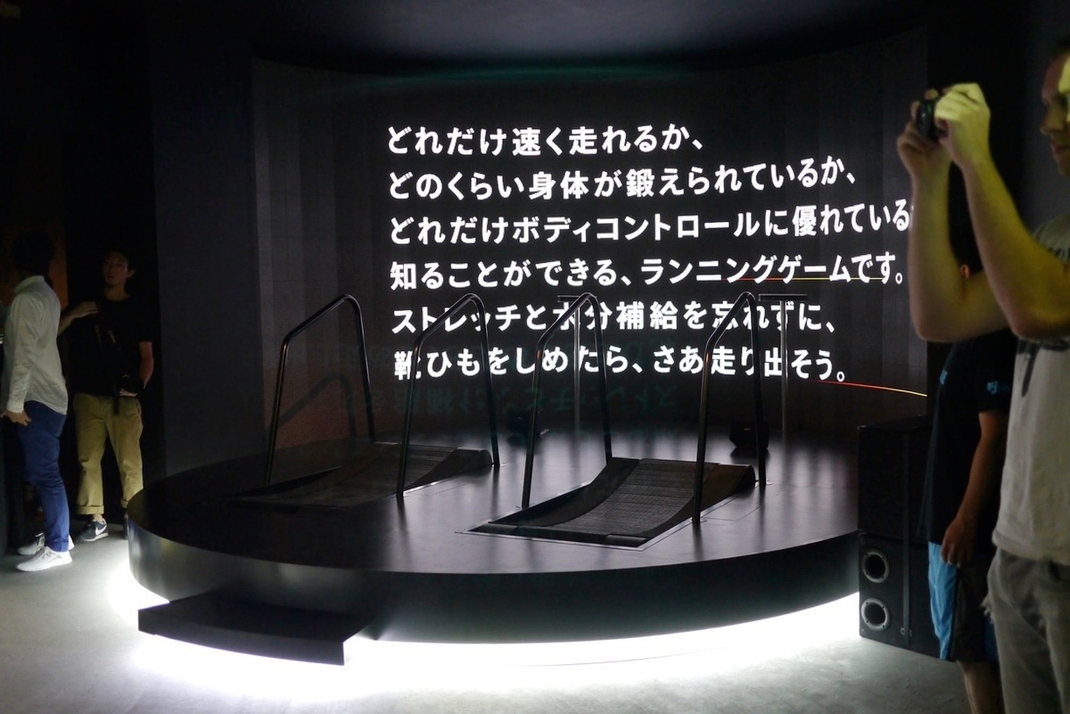 Two treadmills on a raised platform with sleek white lighting and japanese characters on the screen in front of it